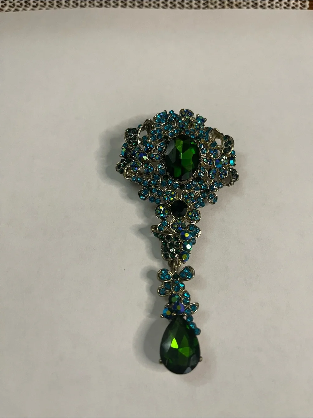 gold-tone teardrop pin featuring a central green crystal surrounded